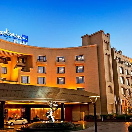 Hotel Radisson Blu Plaza Delhi Airport Nuova Delhi Esterno foto The photo shows the exterior of the Radisson Blu hotel, featuring a modern architectural design. The building is well-lit, with warm lighting highlighting its structure during what appears to be dusk. There is a large entrance area with a canopy, and