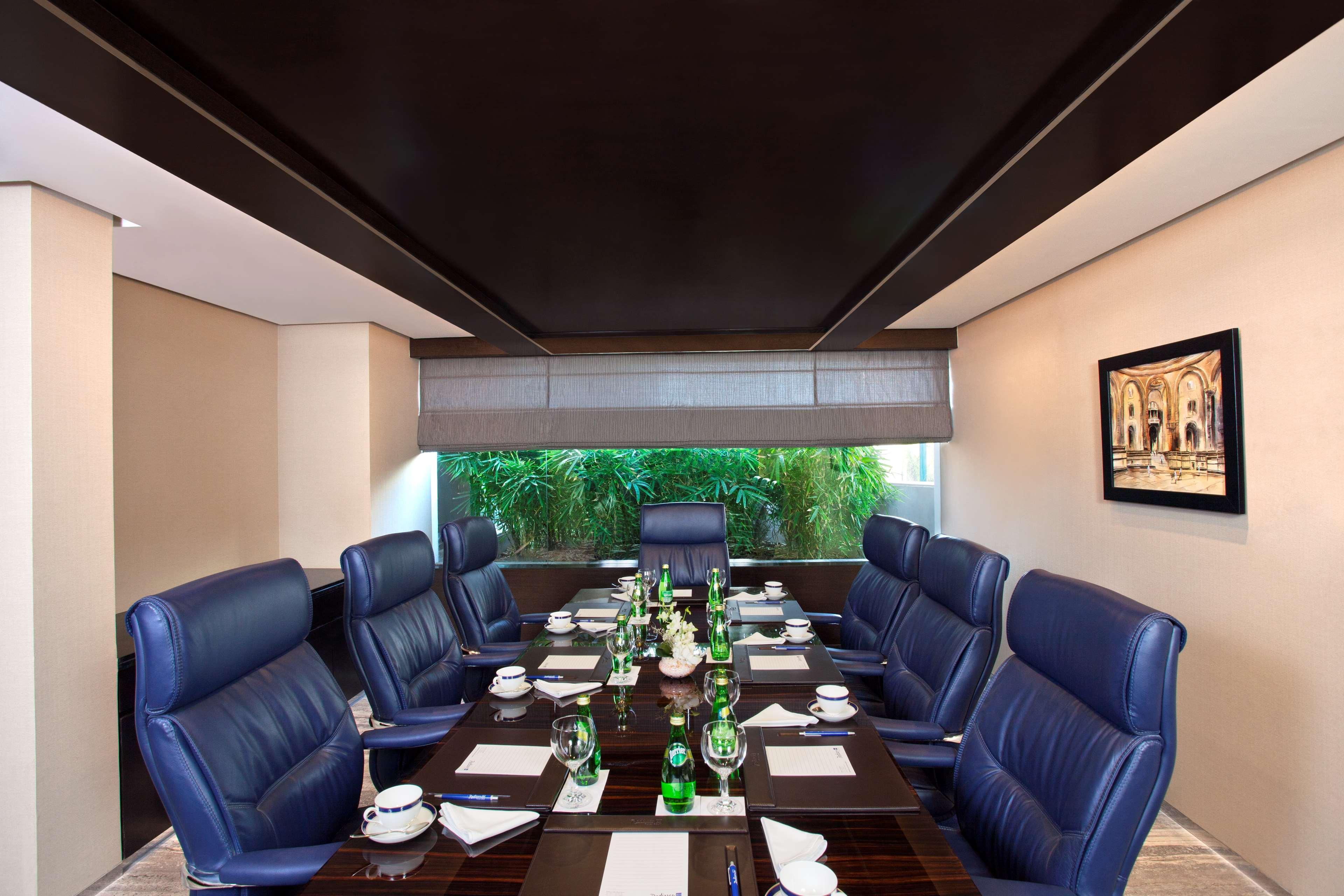 Hotel Radisson Blu Plaza Delhi Airport Nuova Delhi Esterno foto The photo shows a modern conference room equipped with a long rectangular table. The table is set with multiple place settings that include notepads and pens, along with glasses and water bottles. Surrounding the table are several blue upholstered ch