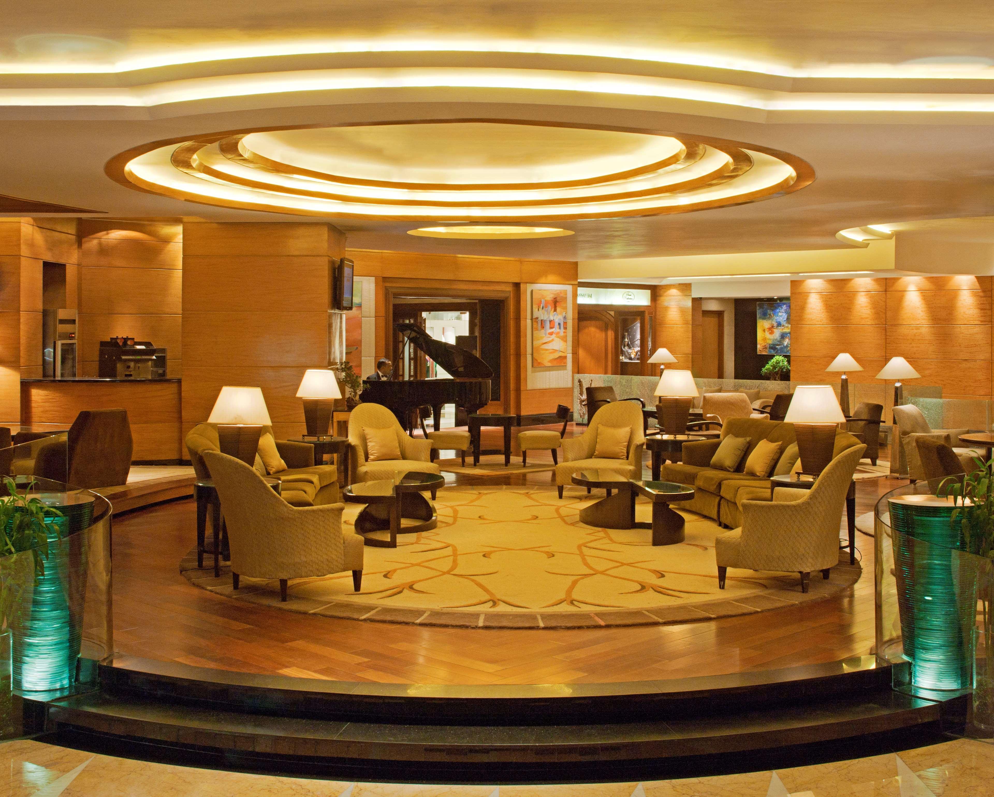 Hotel Radisson Blu Plaza Delhi Airport Nuova Delhi Esterno foto The photo shows a hotel lobby or lounge area, characterized by warm, inviting lighting and a modern design. The space features a circular ceiling with soft, recessed lights that create an ambient atmosphere. There are several comfortable seating arra