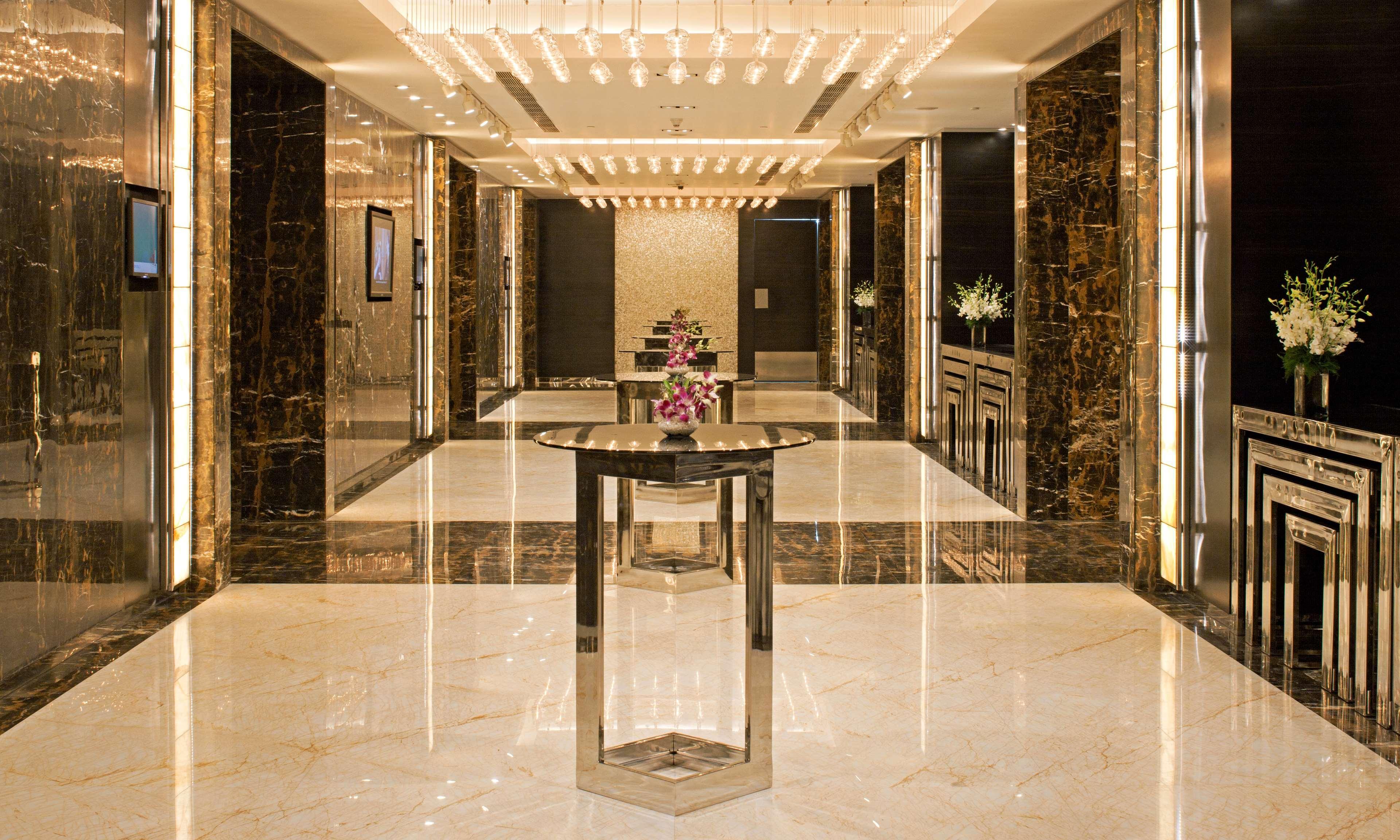 Hotel Radisson Blu Plaza Delhi Airport Nuova Delhi Esterno foto The photo depicts an elegant and modern interior space, likely a lobby or reception area. The flooring is shiny marble, and the walls are adorned with dark marble panels, contributing to a luxurious ambiance. Soft, warm lighting is provided by numero