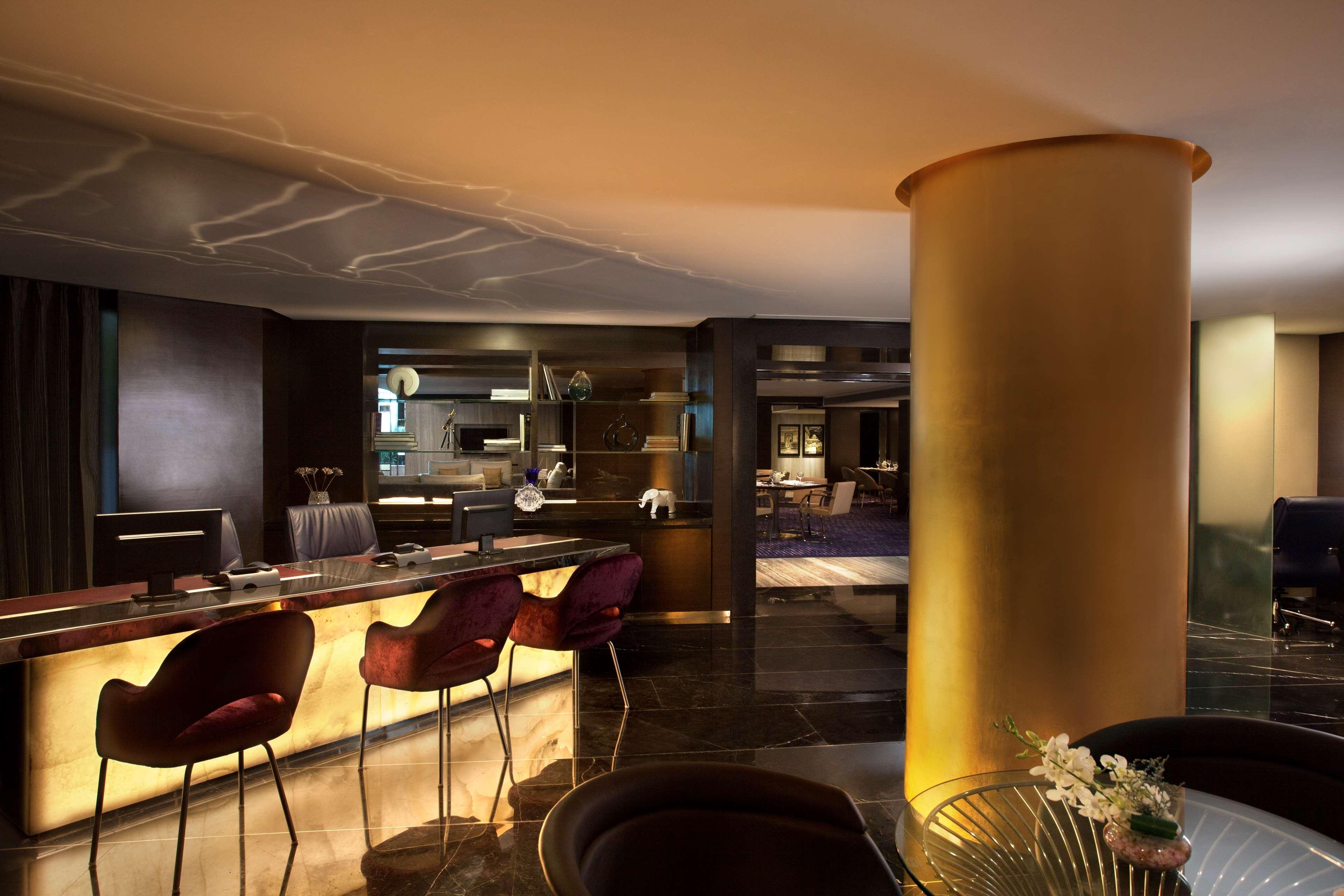 Hotel Radisson Blu Plaza Delhi Airport Nuova Delhi Esterno foto The photo showcases a modern and stylish interior of a lobby or lounge area. It features a reception counter with a warm, illuminated surface, complementing elegant bar-style seating with plush, dark-colored chairs. In the background, there are vario