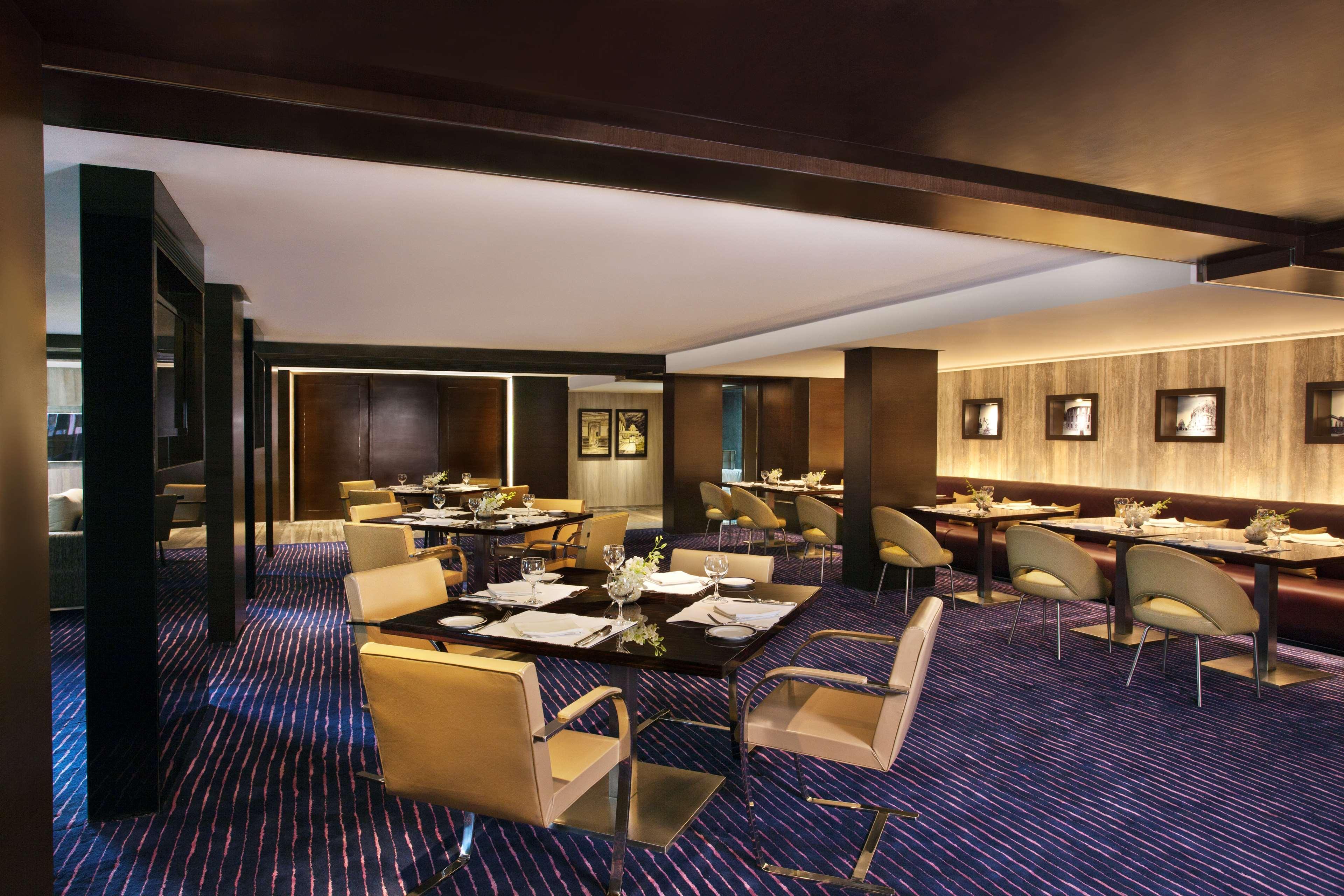 Hotel Radisson Blu Plaza Delhi Airport Nuova Delhi Esterno foto The image shows an elegant dining room with a modern and sophisticated design. It features several tables set for dining, with stylish chairs around them. The decor includes wooden paneling and soft, ambient lighting, creating a warm atmosphere. The 