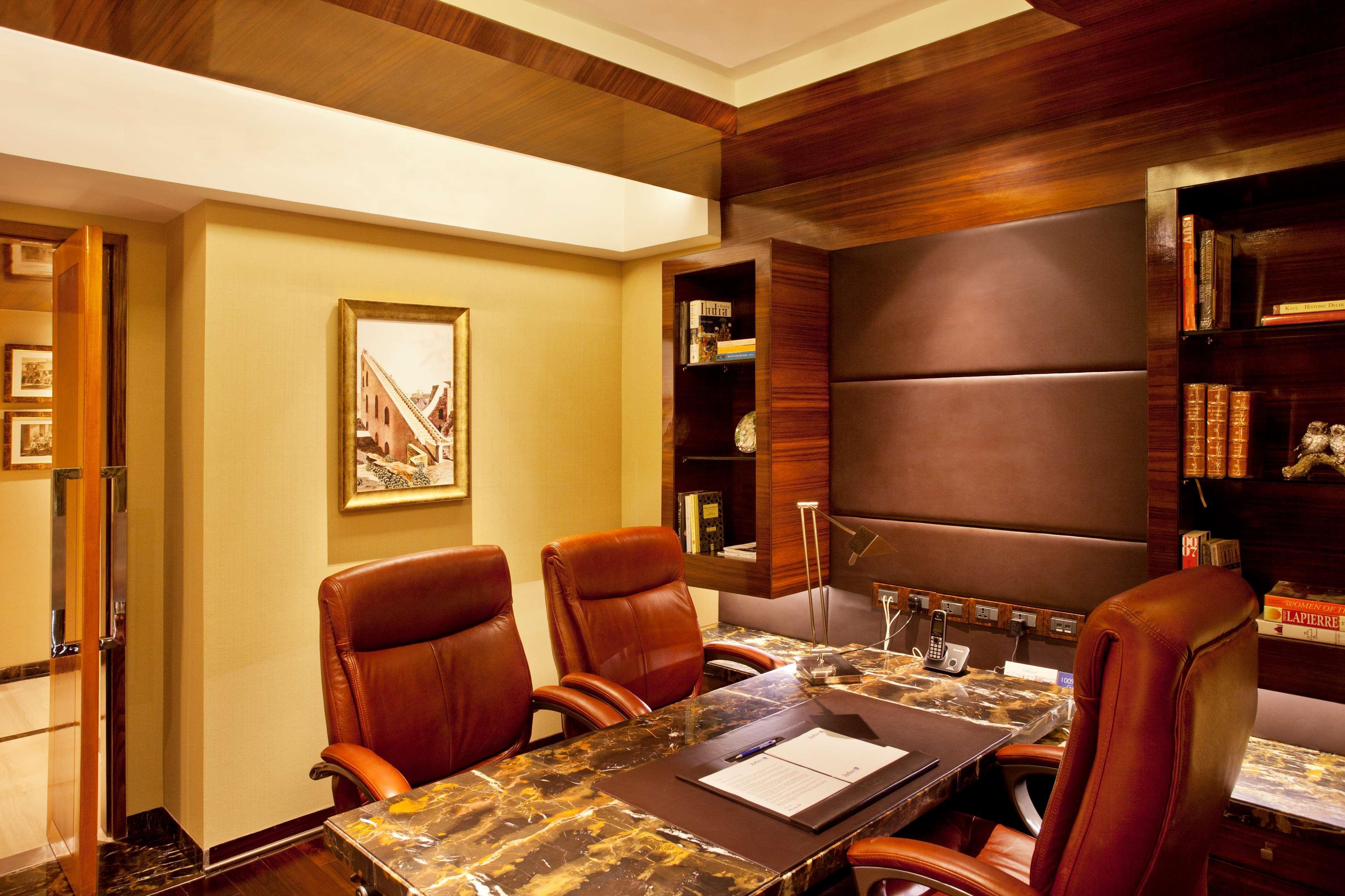 Hotel Radisson Blu Plaza Delhi Airport Nuova Delhi Esterno foto The photo shows a stylish office space. It features a wooden desk with a marble top positioned in the center. There are three brown leather chairs around the desk, suggesting a professional and comfortable environment. The walls are elegantly designe
