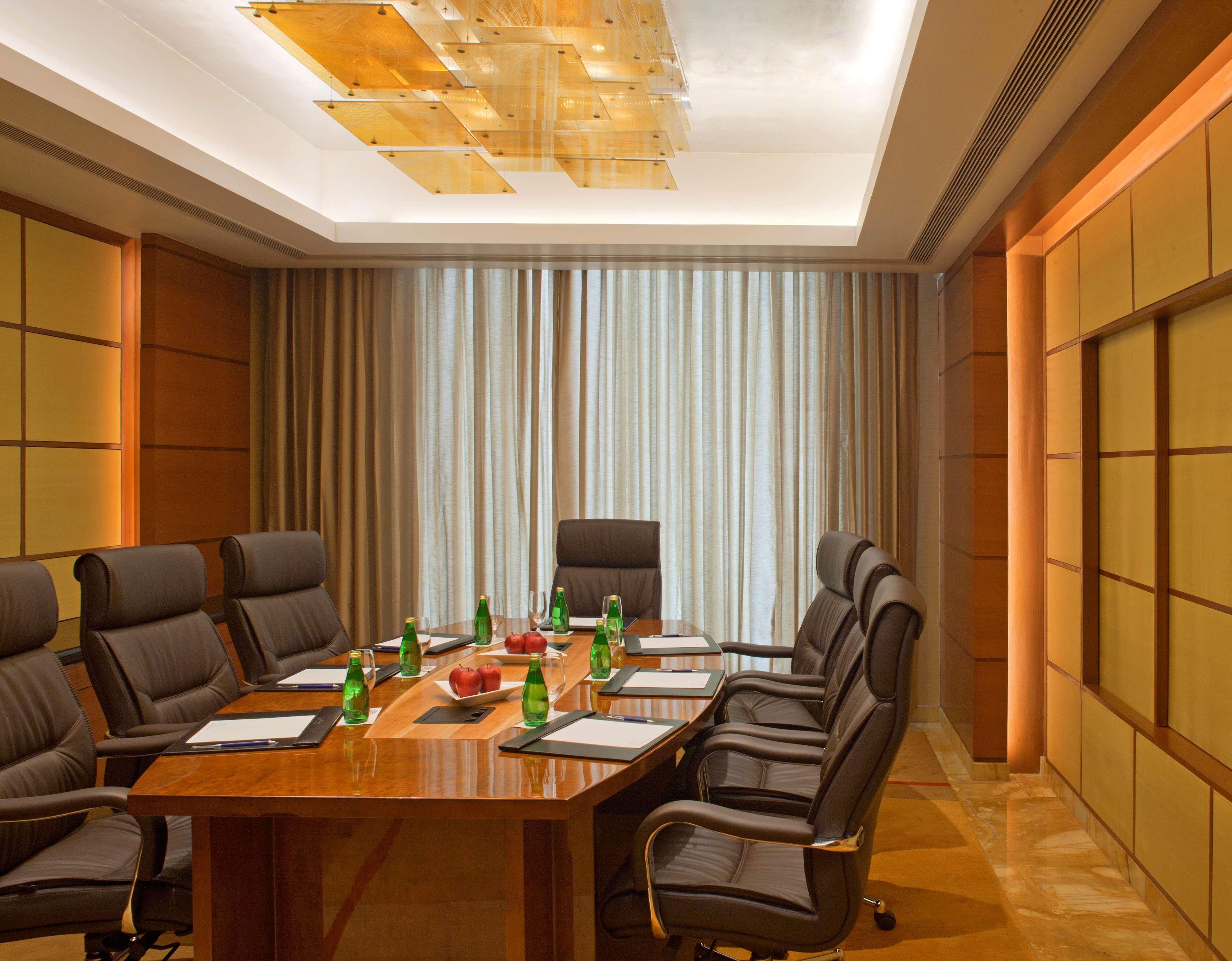Hotel Radisson Blu Plaza Delhi Airport Nuova Delhi Esterno foto The photo shows a modern conference room. The room features a large wooden table surrounded by several comfortable chairs. On the table, there are green bottles and possibly some stationery items. The walls are designed with wooden panels and there i