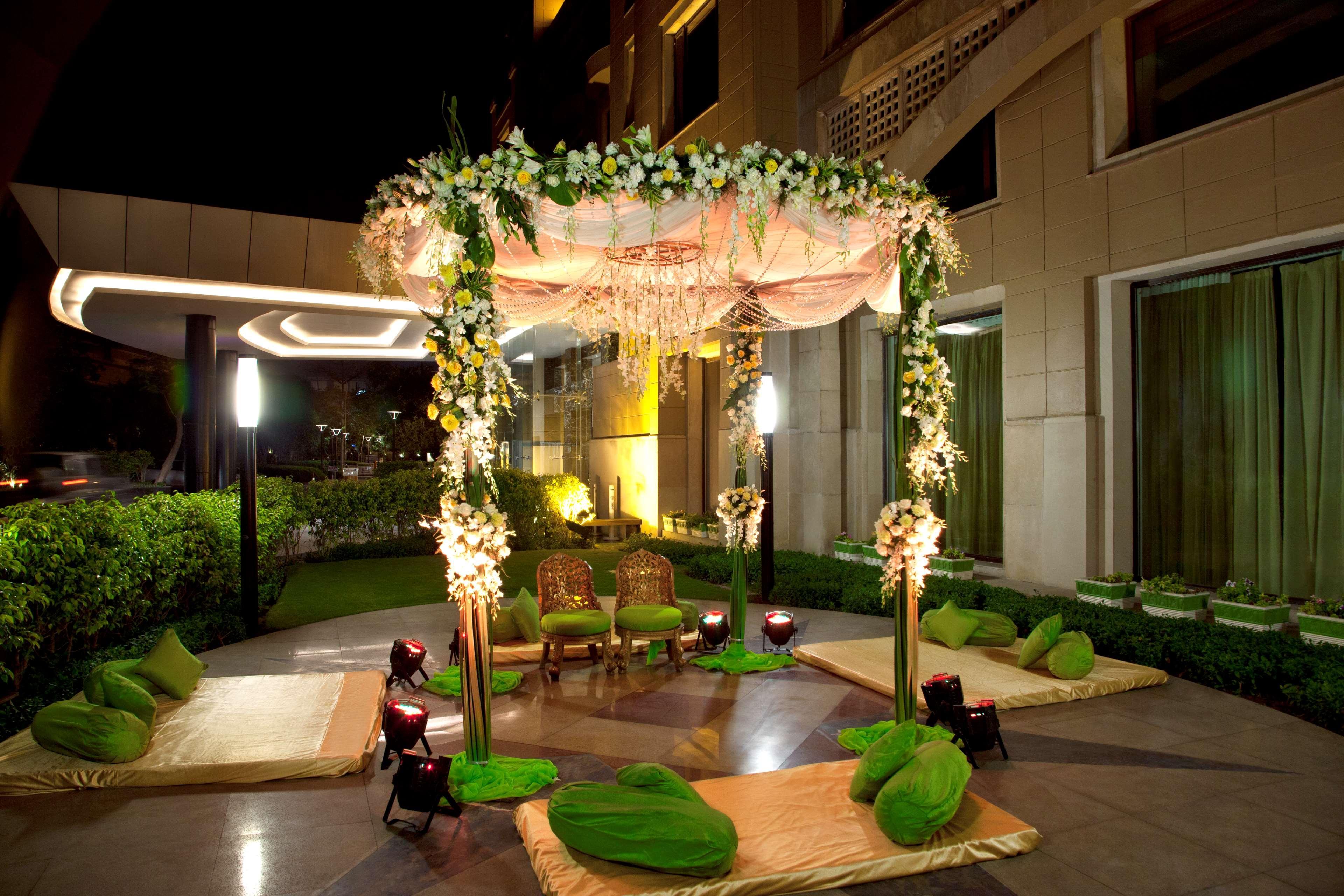 Hotel Radisson Blu Plaza Delhi Airport Nuova Delhi Esterno foto The photo depicts a beautifully arranged outdoor setting, ideal for a celebration or event. In the center, there is a decorated canopy adorned with flowers and drapes, creating a romantic and festive atmosphere. Below the canopy, two ornate chairs ar