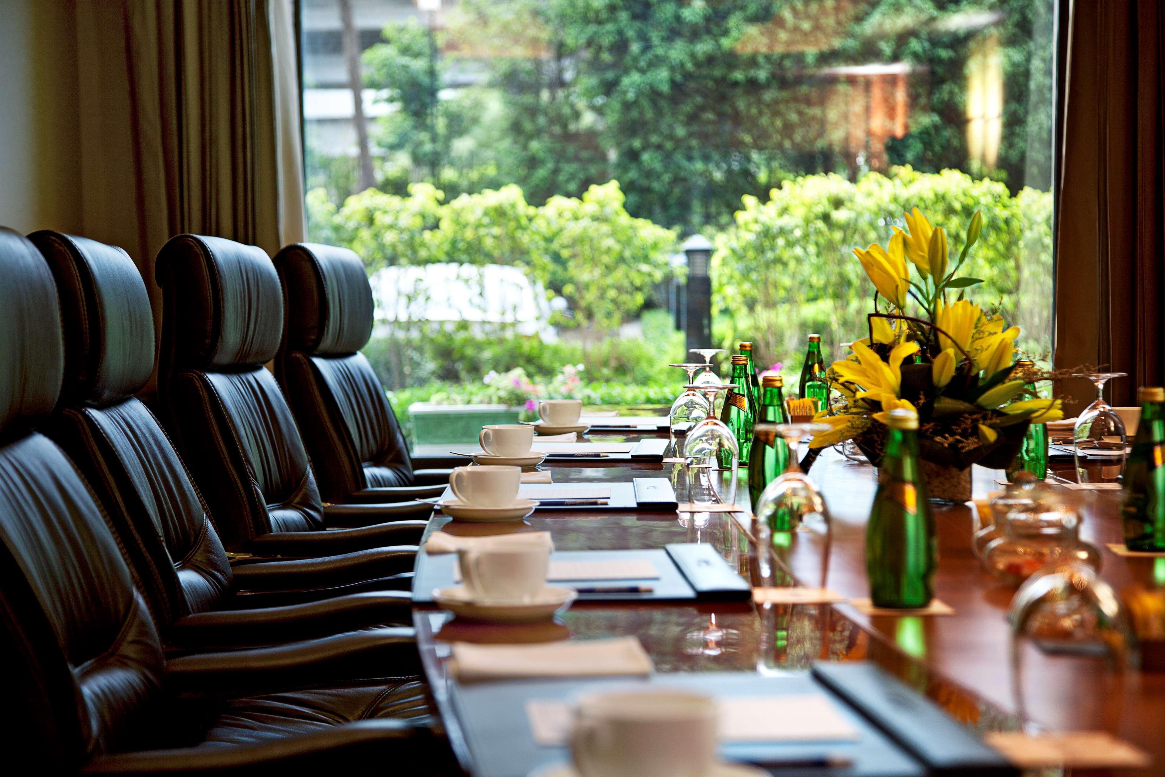 Hotel Radisson Blu Plaza Delhi Airport Nuova Delhi Esterno foto The photo shows a conference room setup with a long, polished wooden table surrounded by several leather chairs. On the table, there are empty tea or coffee cups, glass water bottles, and a few clear glass containers. At one end of the table, there's