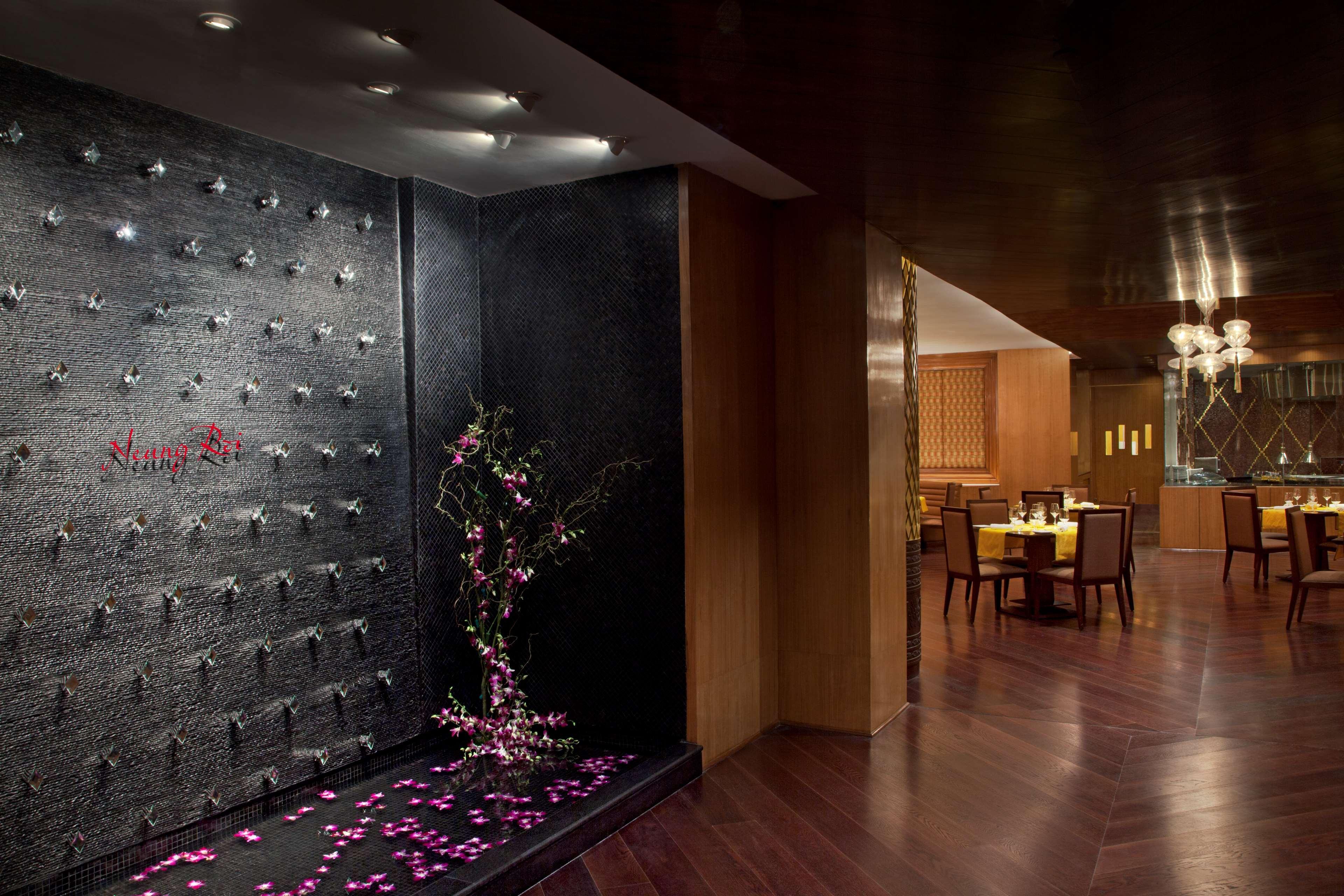 Hotel Radisson Blu Plaza Delhi Airport Nuova Delhi Esterno foto The photo shows a sophisticated interior space, likely a restaurant or a dining area. On one side, there's an artistic wall featuring dark stone or tile, embellished with small light fixtures and a decorative pattern. In front of the wall, there are 