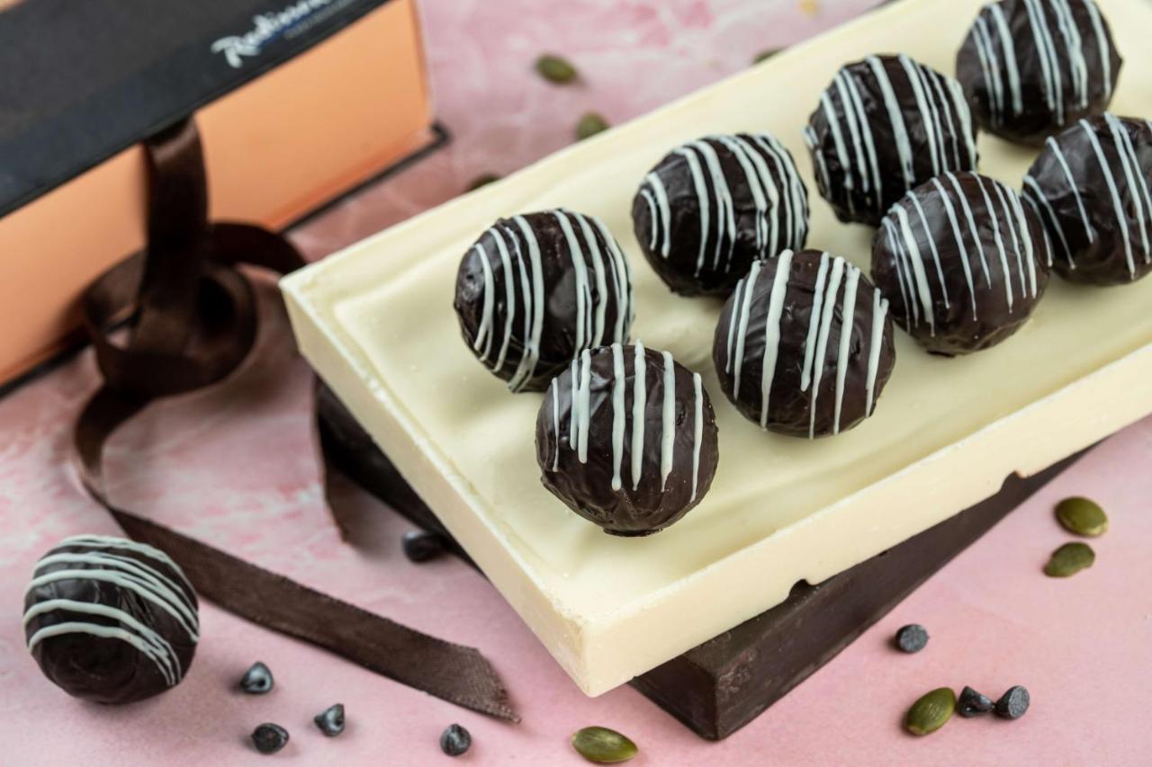 Hotel Radisson Blu Plaza Delhi Airport Nuova Delhi Esterno foto The photo shows an assortment of chocolate truffles arranged neatly on a rectangular chocolate base. The truffles are round and have a glossy dark chocolate coating, decorated with white chocolate stripes. They are placed on a light-colored chocolate