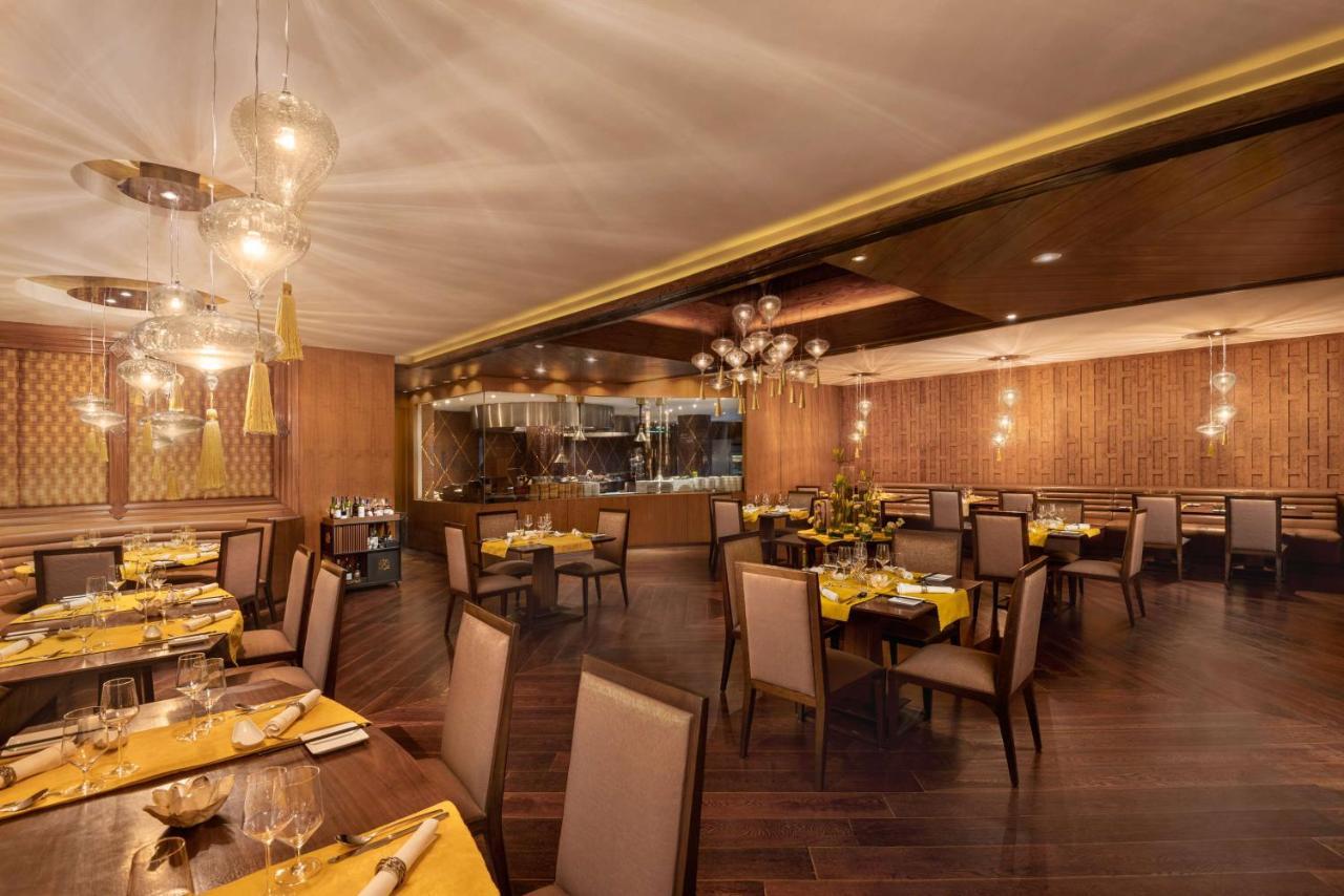Hotel Radisson Blu Plaza Delhi Airport Nuova Delhi Esterno foto The photo shows a stylish restaurant interior. The space features wooden flooring and elegant decor. Tables are set with yellow tablecloths and fine diningware. There are comfortable chairs arranged around the tables, and soft ambient lighting from h