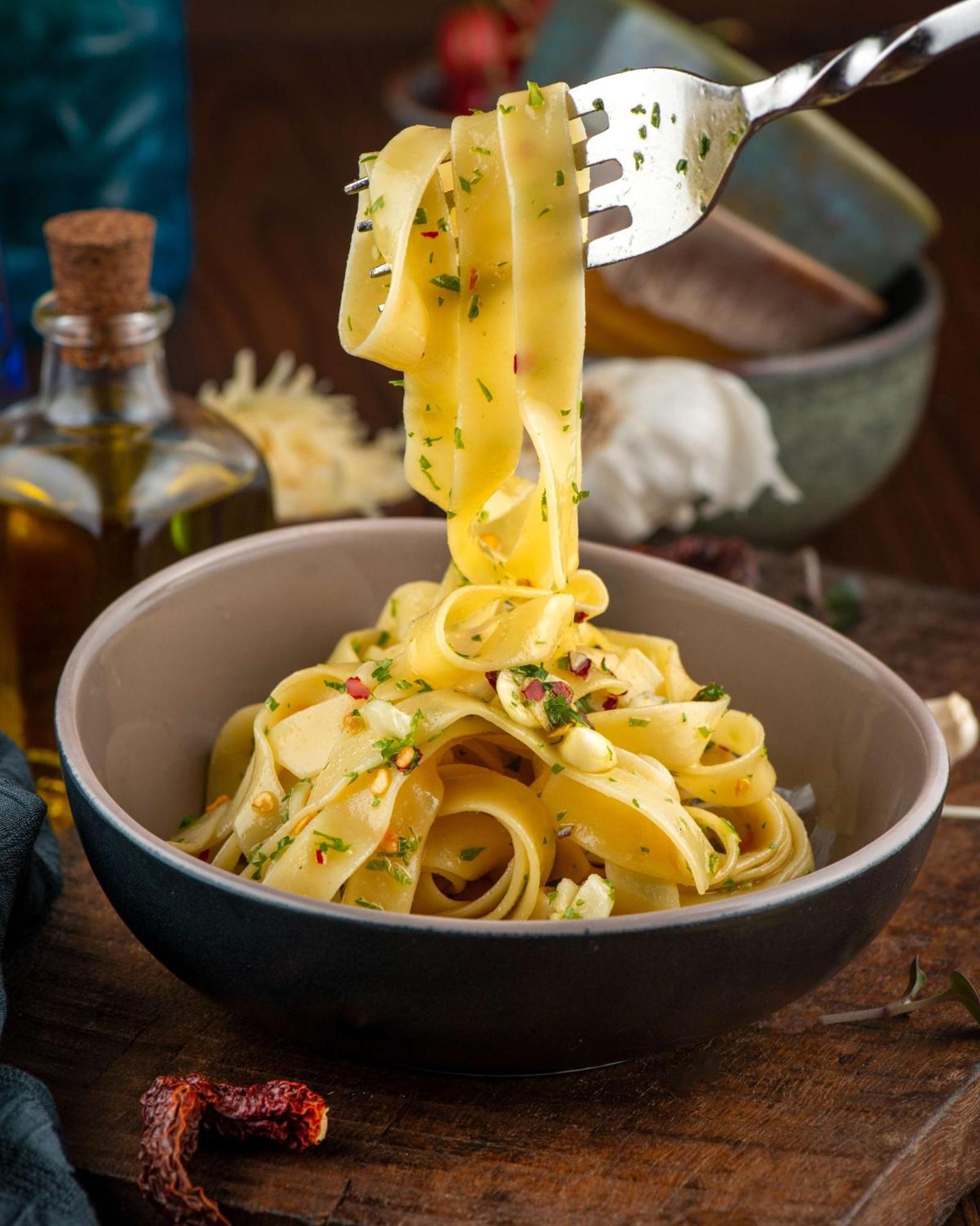 Hotel Radisson Blu Plaza Delhi Airport Nuova Delhi Esterno foto The photo shows a bowl of pasta, specifically fettuccine, that is garnished with herbs and possibly some finely chopped ingredients. A portion of the pasta is being lifted with a fork, showcasing its smooth and flat texture. The background includes a