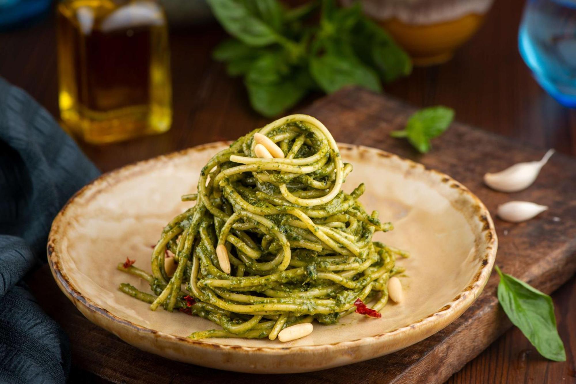 Hotel Radisson Blu Plaza Delhi Airport Nuova Delhi Esterno foto The photo displays a serving of spaghetti pasta dressed in a vibrant green pesto sauce. It is elegantly plated in a round, shallow dish and topped with pine nuts. The background features fresh basil leaves and a bottle of olive oil, adding to the rus