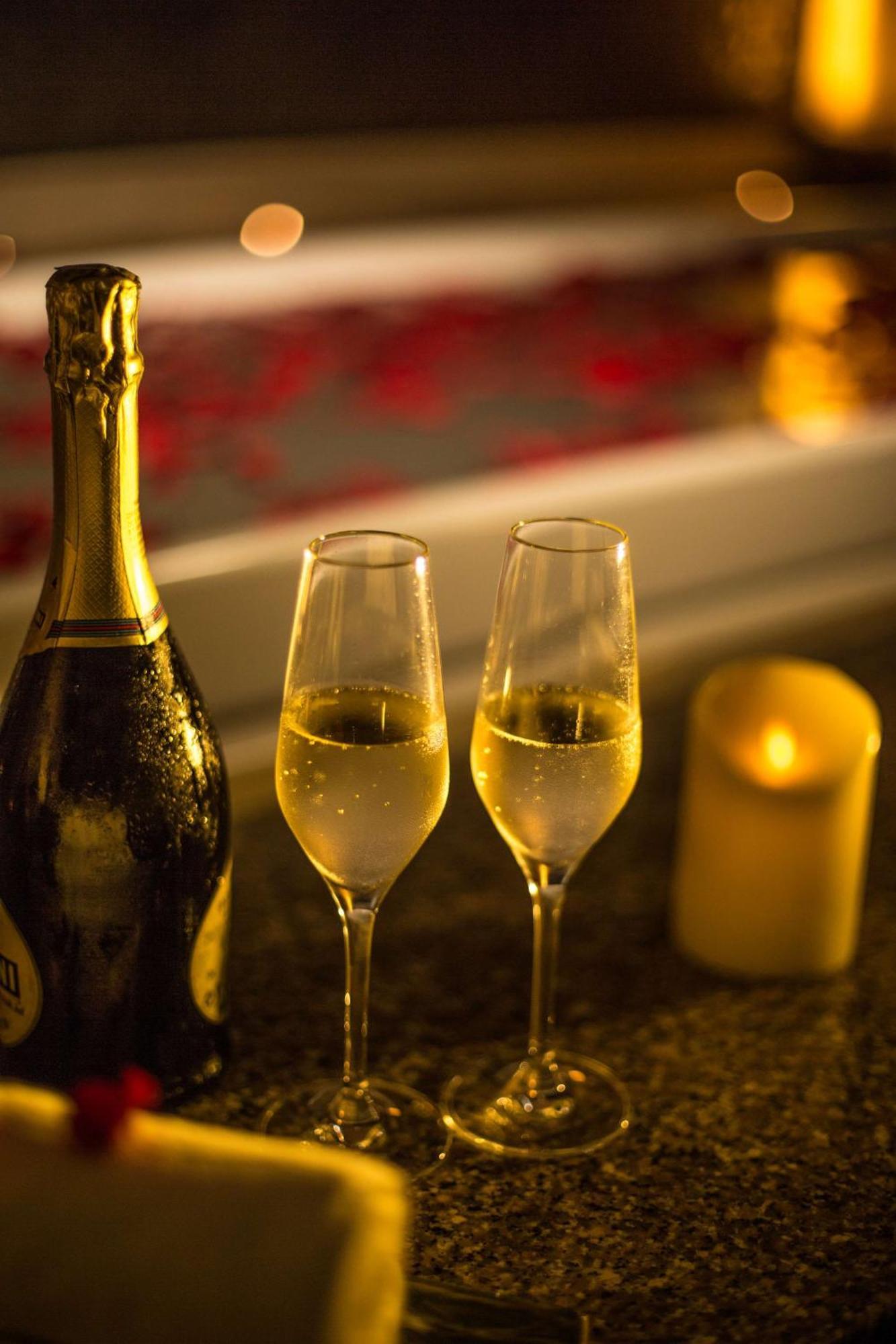 Hotel Radisson Blu Plaza Delhi Airport Nuova Delhi Esterno foto The photo features a bottle of sparkling wine and two fluted glasses filled with the drink. The glasses are placed on a countertop, and a lit candle is nearby, creating a warm and inviting atmosphere. The background has hints of red, possibly from ro