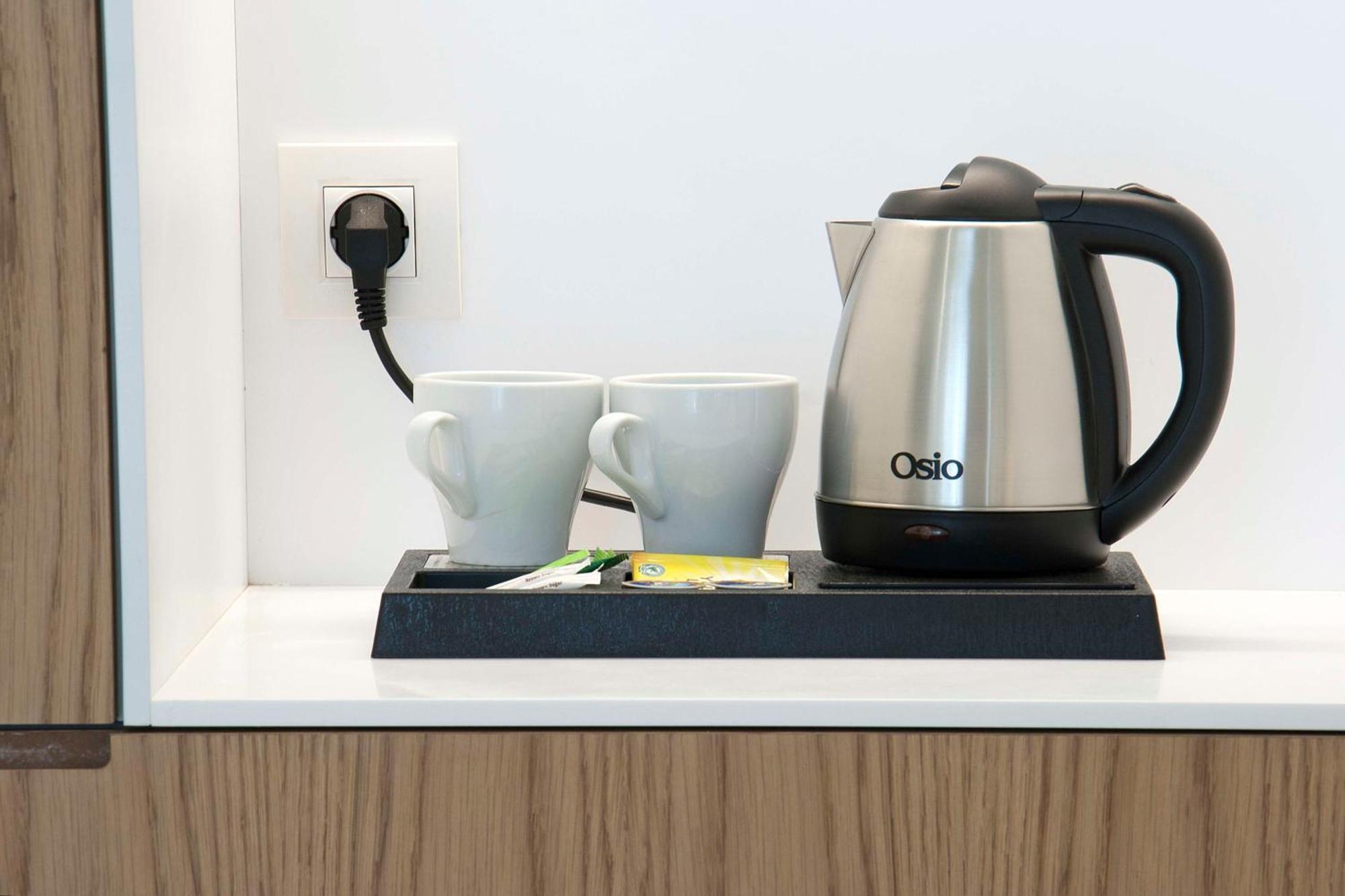 Hotel Radisson Blu Plaza Delhi Airport Nuova Delhi Esterno foto The photo shows an electric kettle placed on a small tray. The kettle is metallic and has a black handle. Next to the kettle, there are two white cups. On the tray, two packets of tea are also visible. Behind the kettle, there is an electrical outlet